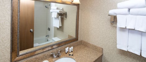 Une salle de bain avec un comptoir en granit, un lavabo blanc, un grand miroir avec éclairage intégré et un porte-serviettes.