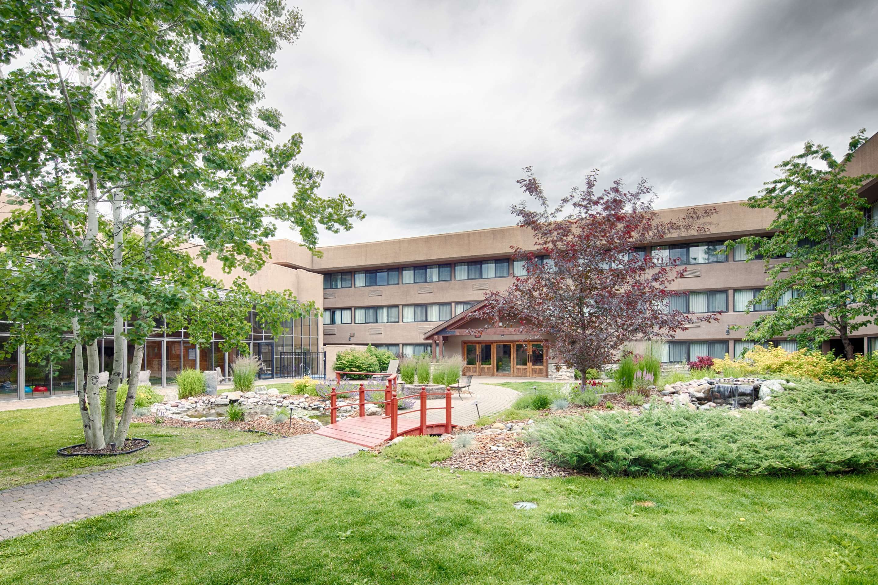A modern building with a brick facade, a landscaped garden with a red bridge, and a small waterfall feature.