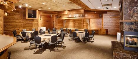 A conference room with round tables and chairs, wooden walls, a stone fireplace, and a ceiling with recessed lighting.