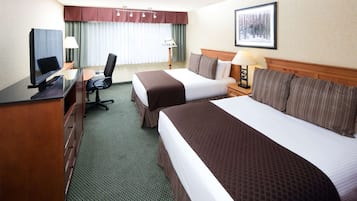 Una habitación de hotel con dos camas, un escritorio con televisión, una silla y una lámpara.