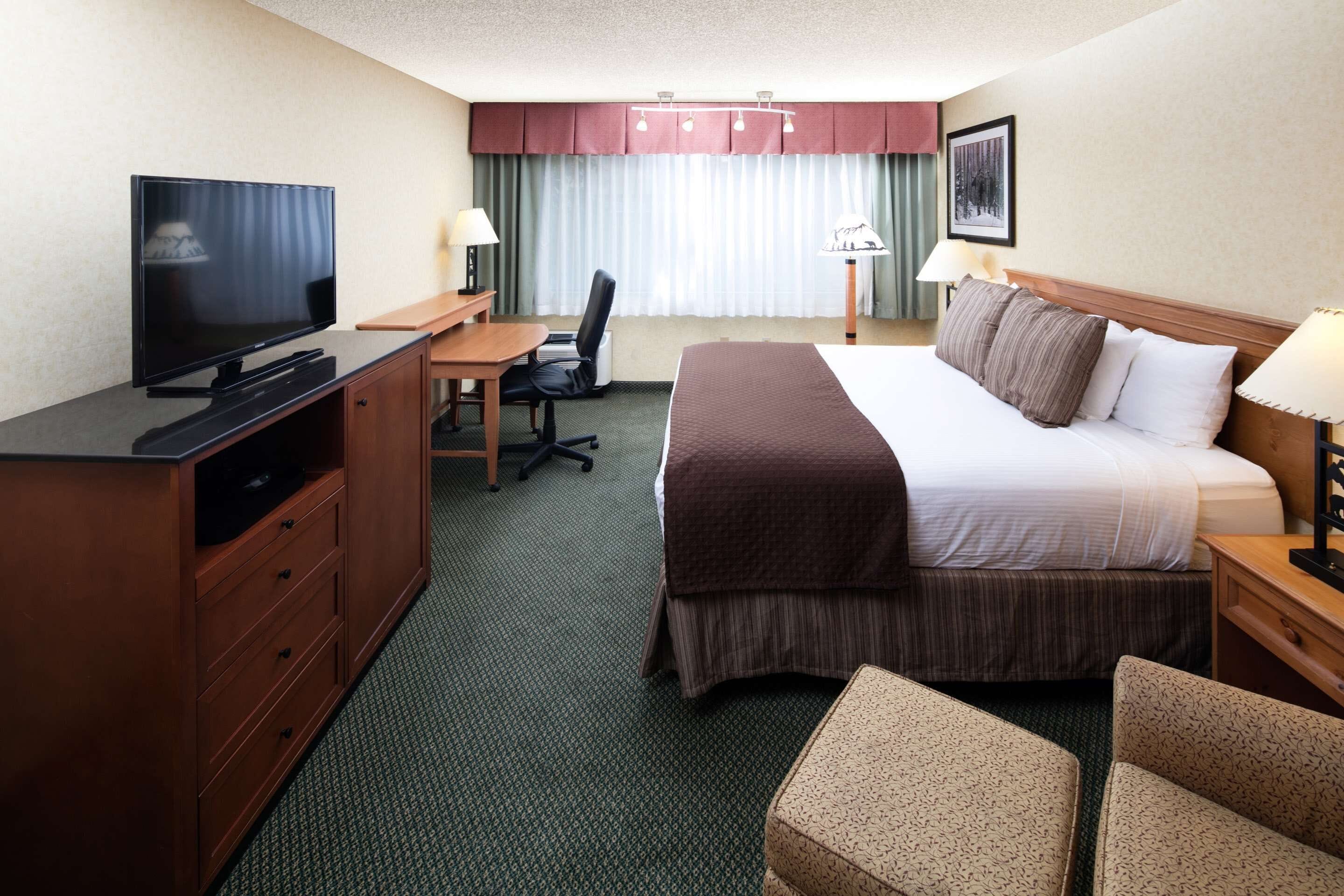 A hotel room with a bed, desk, chair, television, and lamps.