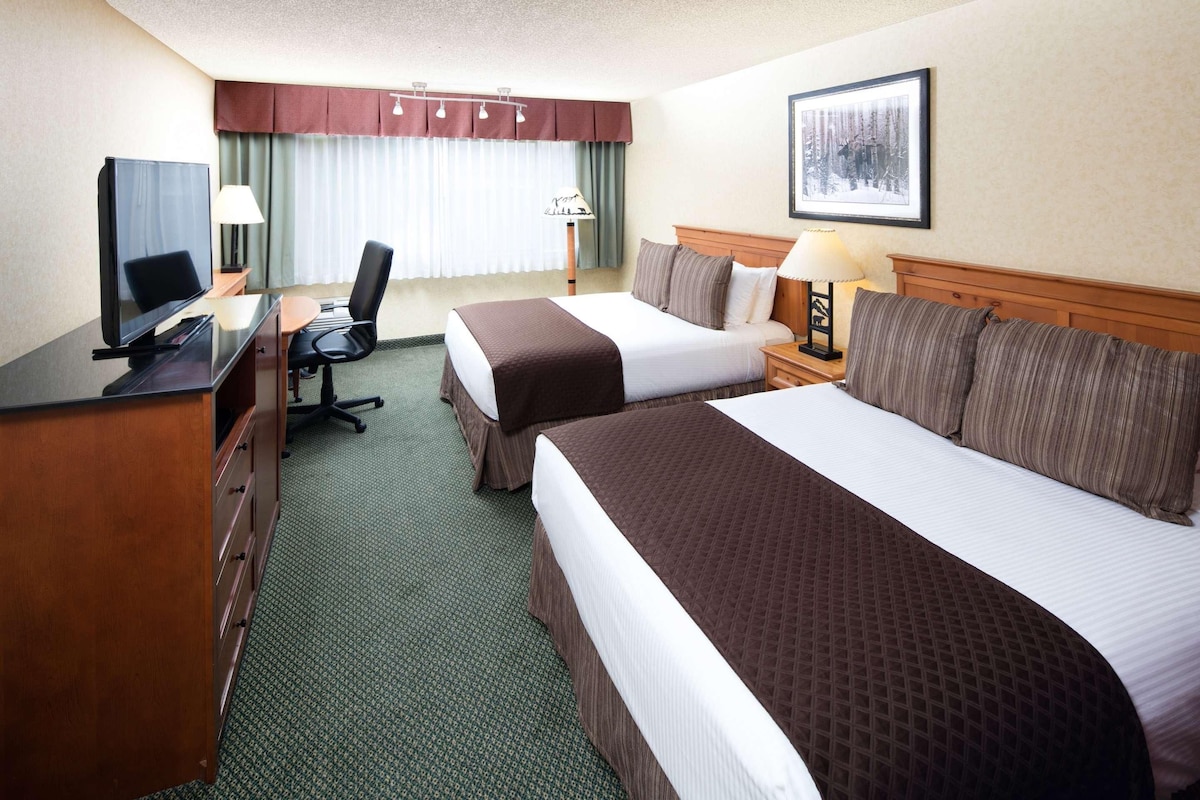 A hotel room with two beds, a desk with a television, a chair, and a lamp.