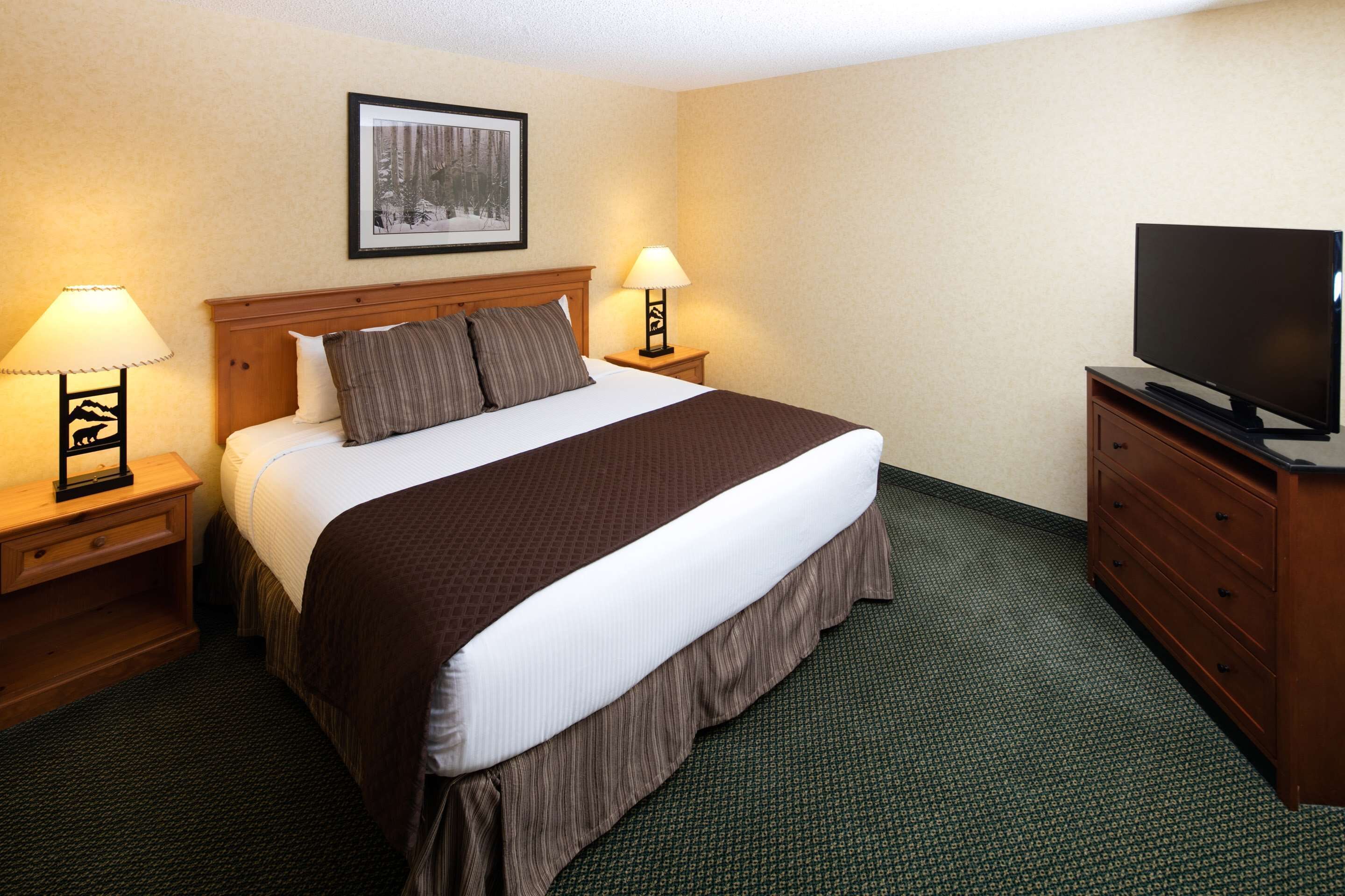 A hotel room with a large bed, two bedside tables with lamps, a television on a wooden cabinet, and a framed picture on the wall.
