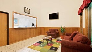 A room with a wooden floor, a red sofa, a brown armchair, a coffee table, a colorful rug, a potted plant, a flat-screen TV, and a wooden door.