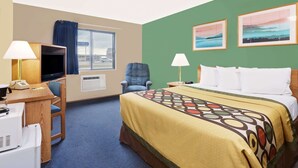 A hotel room with a bed, desk, chair, TV, and two paintings on the wall.