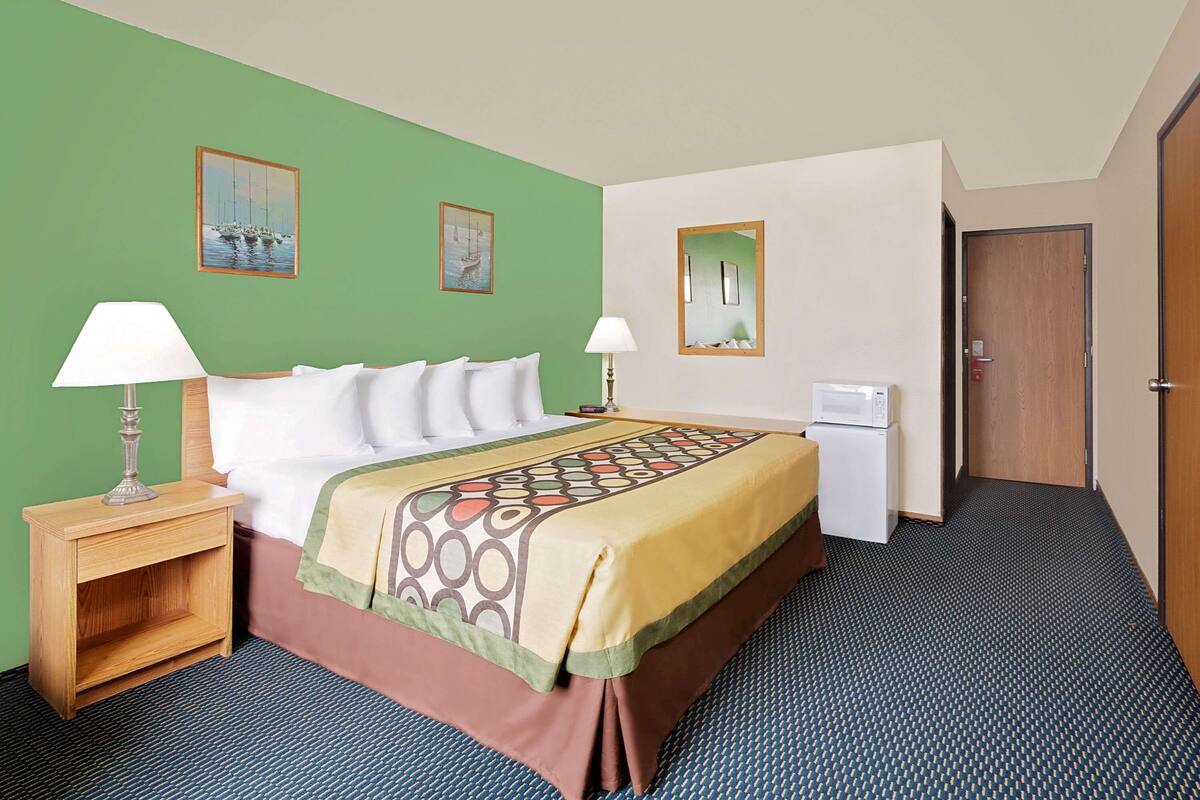 Hotelkamer met een bed, twee nachtkastjes met lampen, een magnetron en een deur.