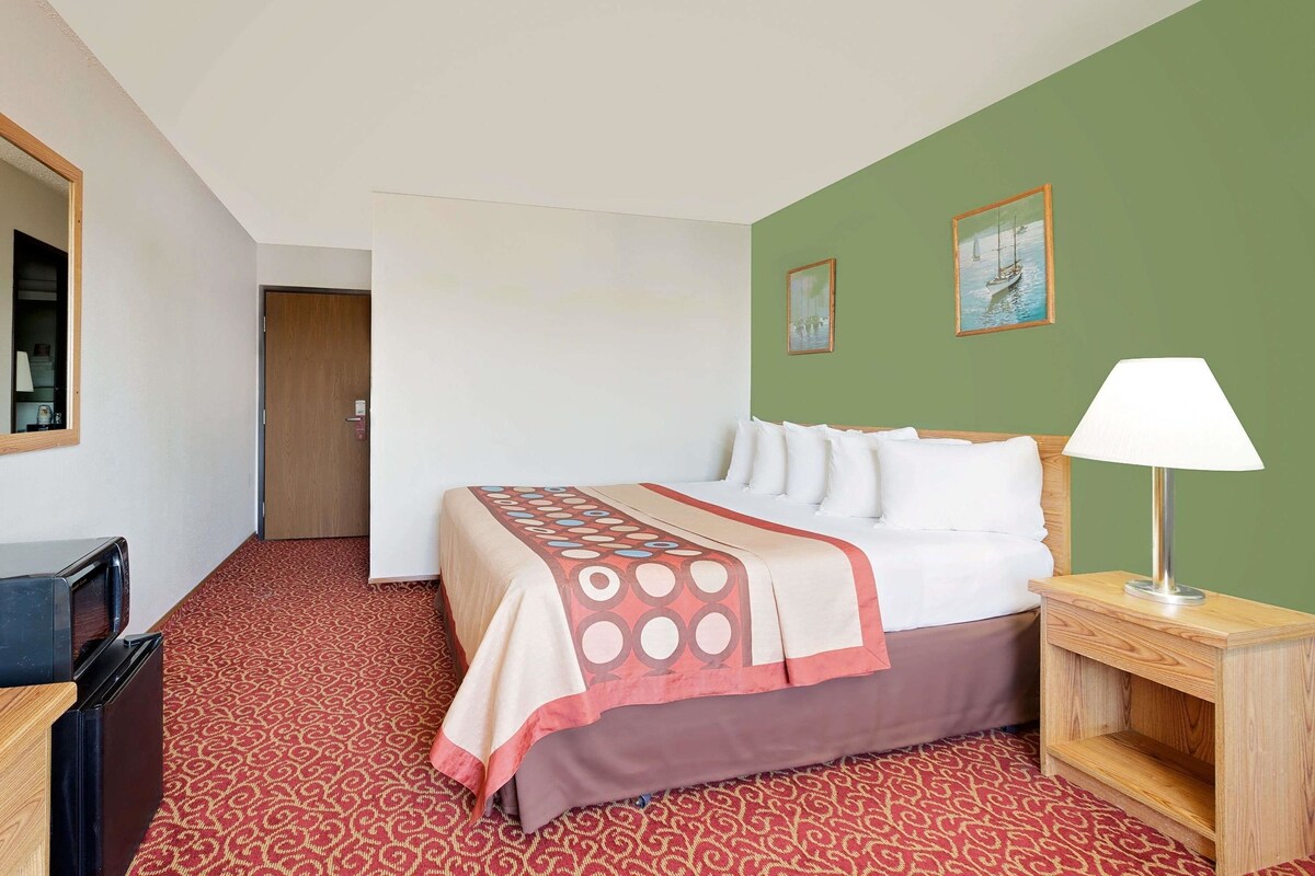 Una habitación de hotel con cama, mesita de noche, lámpara, espejo y puerta.
