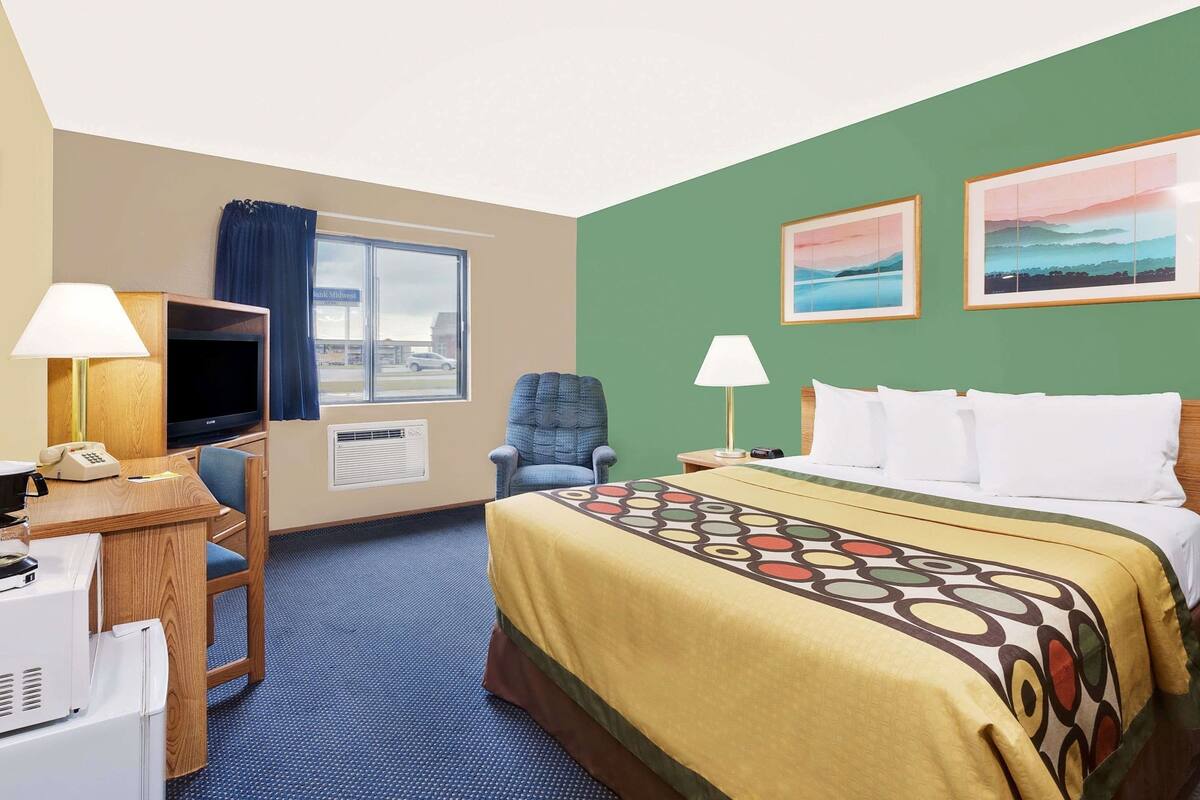 Een hotelkamer met een bed, twee lampen, een bureau met telefoon, een stoel, een televisie en een raam met uitzicht op een gebouw.