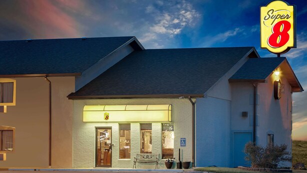 A Super 8 hotel with a well-lit entrance, a bench outside, and a clear view of the sky.