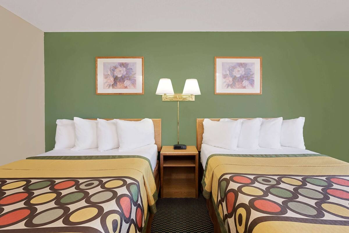 Une chambre d’hôtel avec deux lits, des murs verts, des œuvres d’art florales encadrées, une table de chevet avec une lampe et une couvre-lit à motifs.