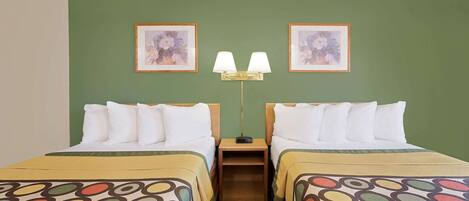 Habitación de hotel con dos camas, paredes verdes, cuadro con motivos florales, mesita de noche con lámpara y edredón estampado.