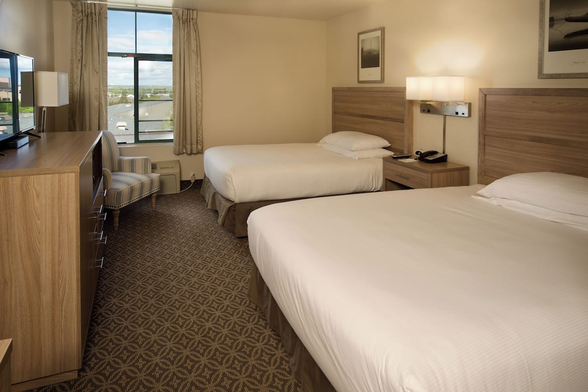 A hotel room with two beds, a desk with a lamp, a chair, and a TV.