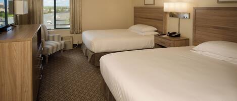 A hotel room with two beds, a desk with a lamp, a chair, and a TV.