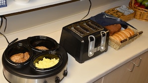 A kitchen counter with a slow cooker, toaster, and bread basket.