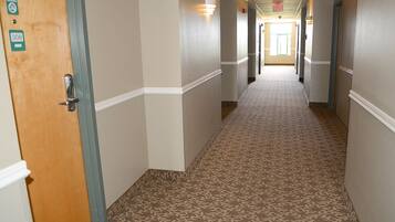 Un pasillo de hotel con alfombra estampada, puertas de madera y lámparas.