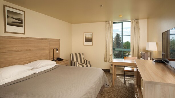 A hotel room with a large bed, a desk with a chair, a television, and a window with curtains.