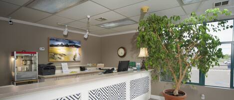 A reception area with a counter, a coffee machine, a clock, and a potted plant.