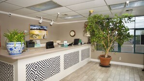 A reception area with a counter, a clock, a potted plant, and patterned wall panels. - The Great Falls Inn by Riversage (Great Falls)