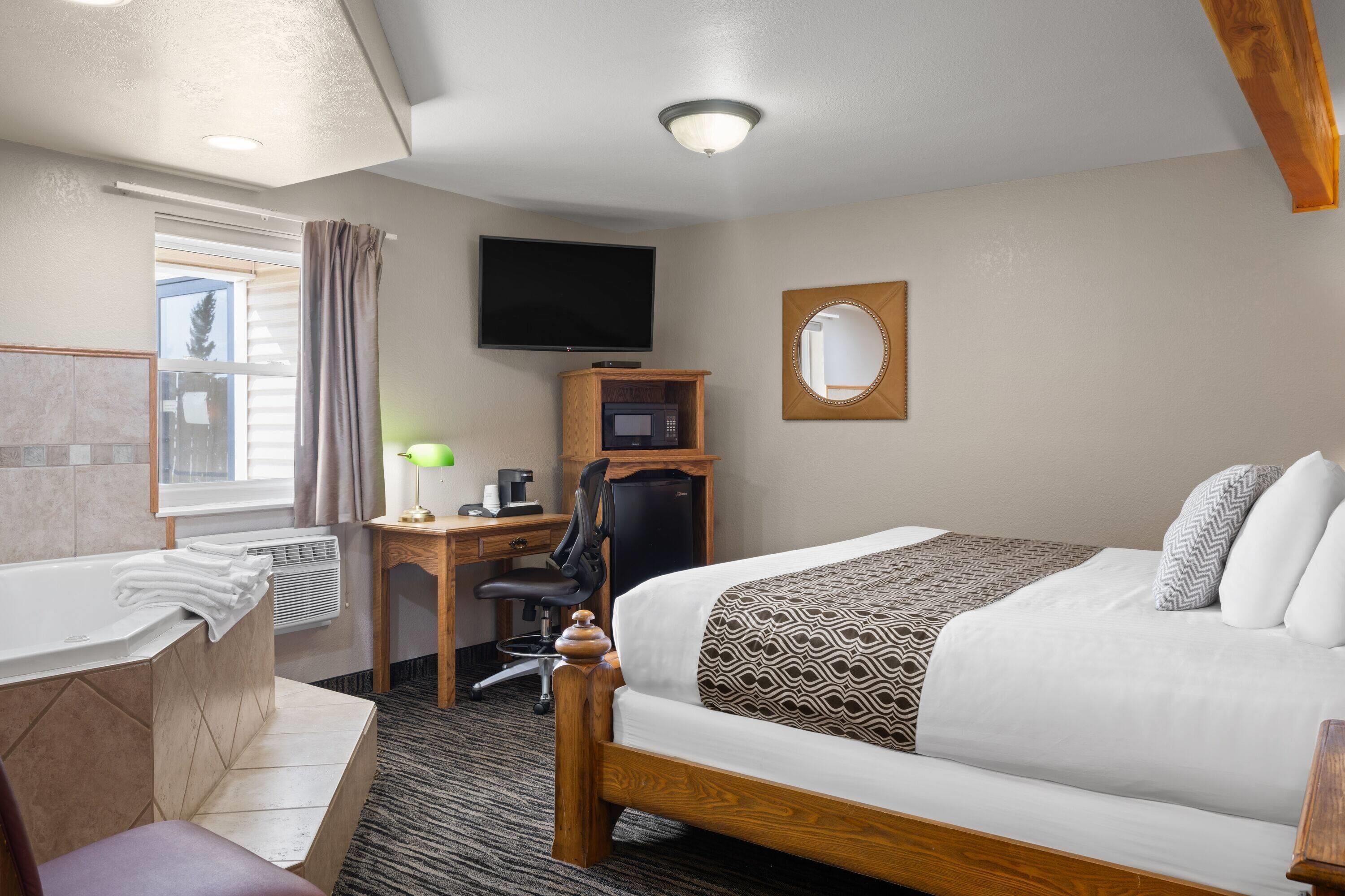A hotel room with a bed, a desk with a computer, a television, a mirror, and a bathroom with a bathtub and towels.