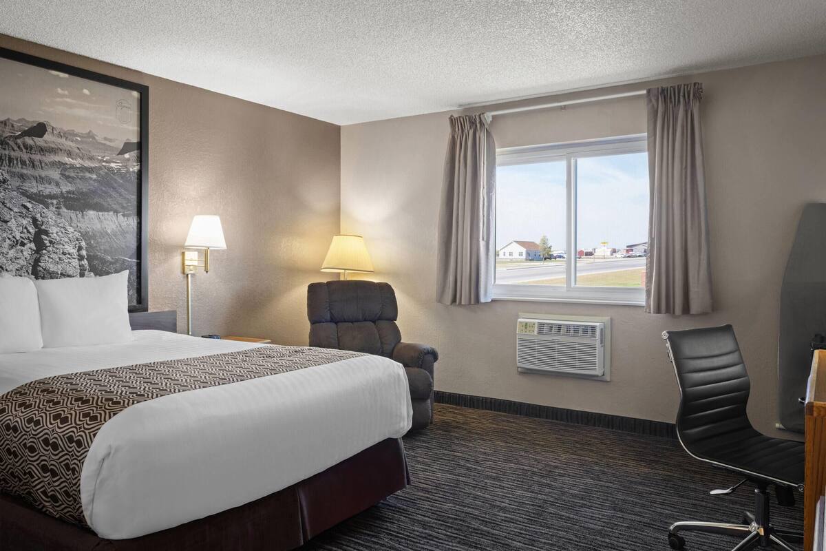 Een hotelkamer met een groot bed, twee stoelen, een bureau, een lamp en een raam met gordijnen.