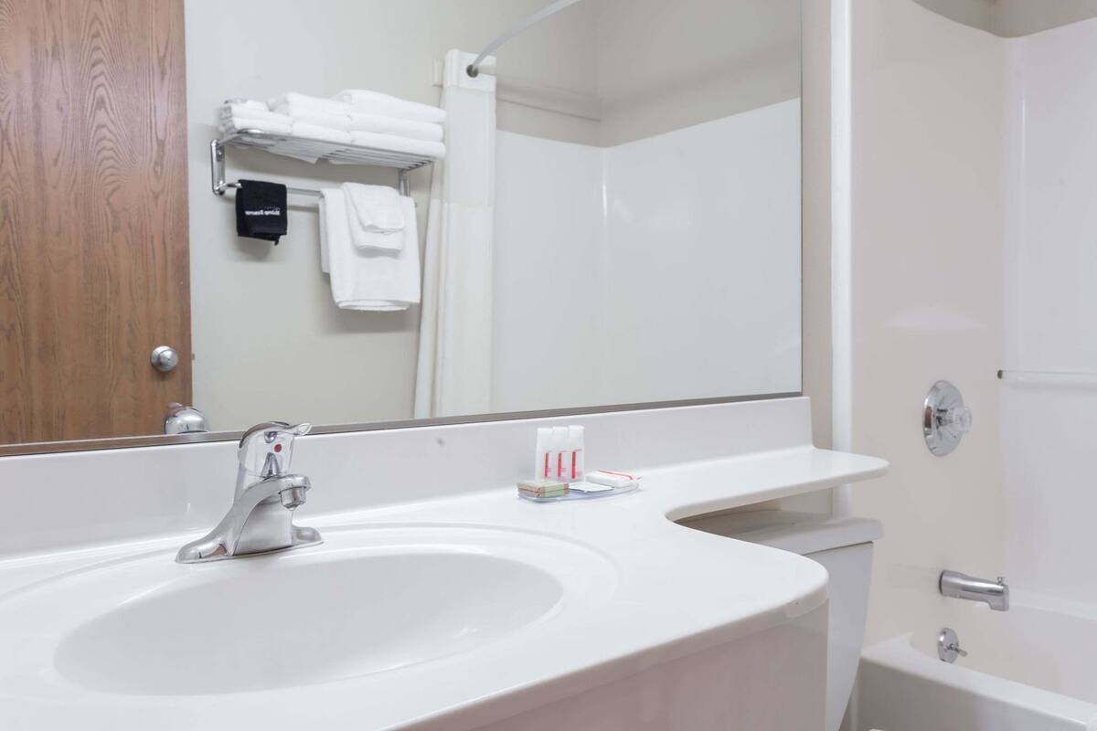 Een badkamer met een wit wastafelmeubel, een spiegel, een douche en een handdoekrek met opgevouwen handdoeken.