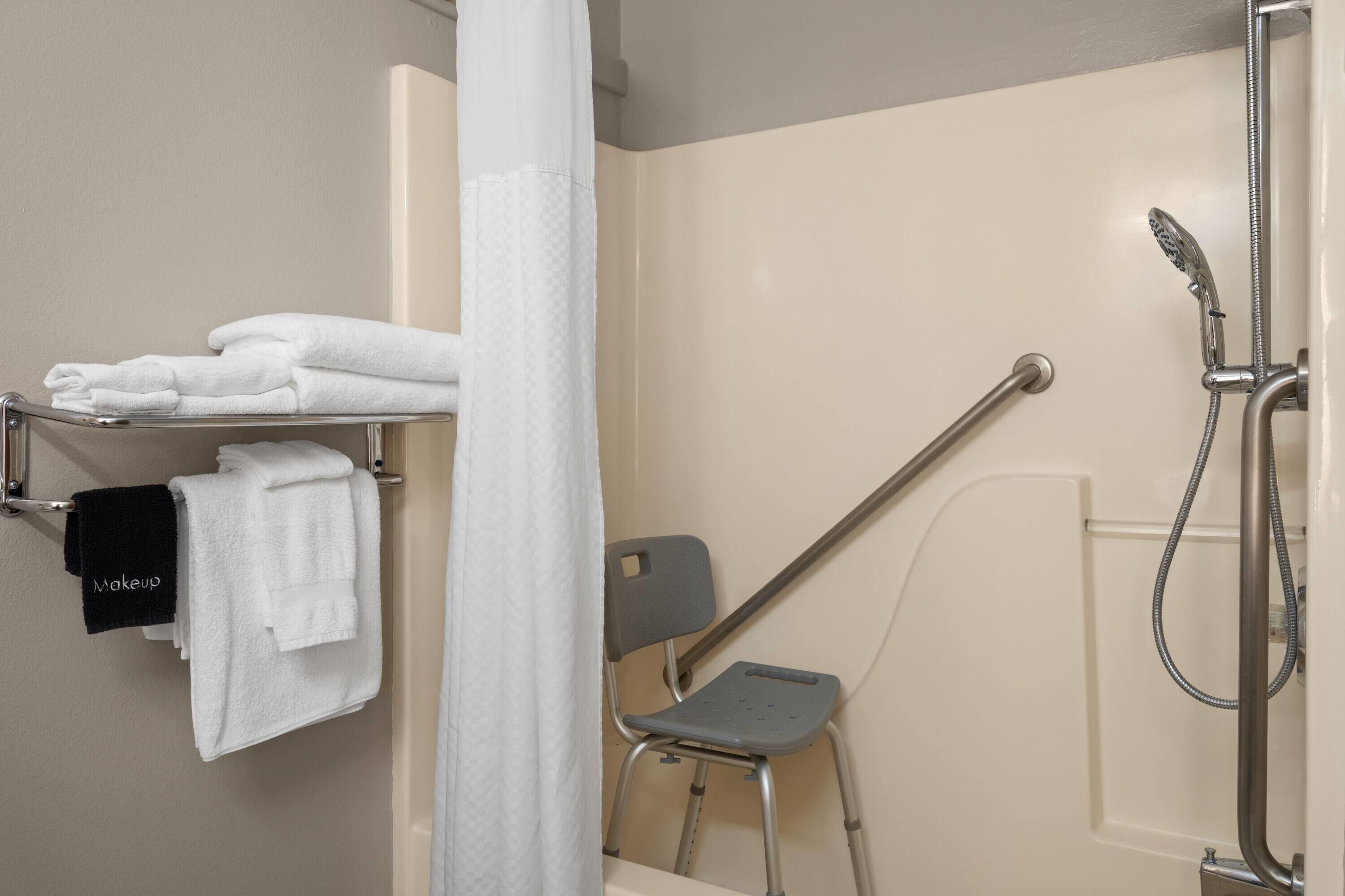 Un espace douche équipé d’une barre d’appui, d’un porte-serviettes avec des serviettes blanches et noires, et d’un pommeau de douche.