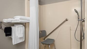 Un espace douche équipé d’une barre d’appui, d’un porte-serviettes avec des serviettes blanches et noires, et d’un pommeau de douche.