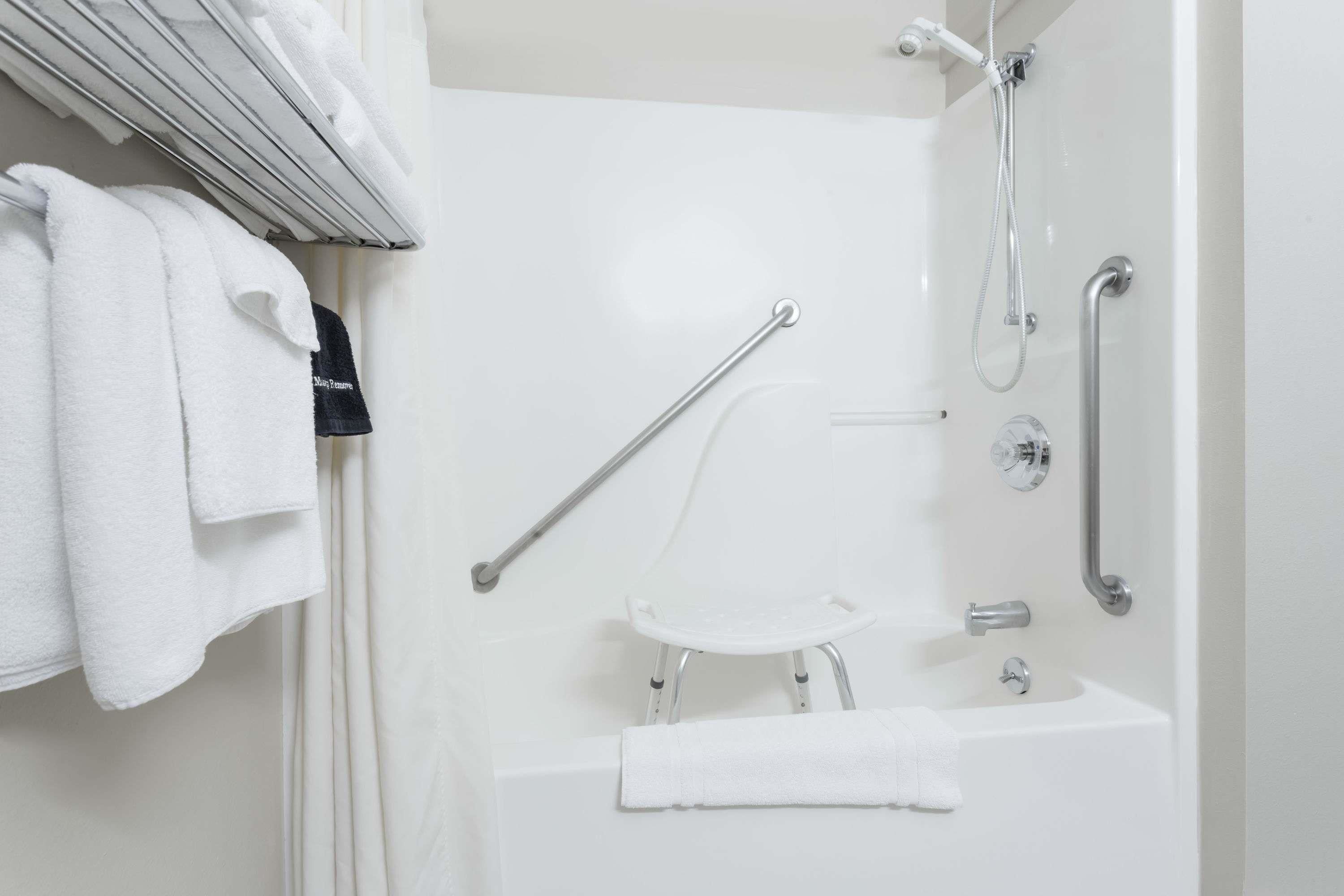Un bagno moderno con doccia a pavimento, maniglie di sostegno, un lavandino bianco e un porta asciugamani.