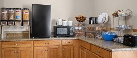 Una cocina con armarios de madera, un refrigerador negro, un microondas y varios recipientes para guardar alimentos.