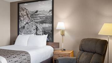 A hotel room with a bed, a chair, a nightstand, a lamp, and a large framed picture on the wall.