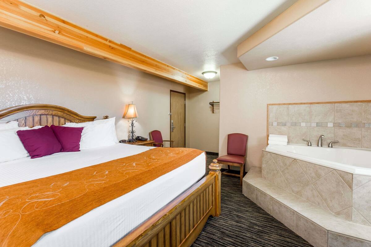 Een hotelkamer met een groot bed, een houten hoofdeinde, een badkamer met bad en een klein bureau met lamp.