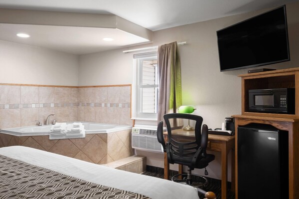 Habitación de hotel con cama, escritorio con silla, televisor, microondas y baño con bañera y ducha.