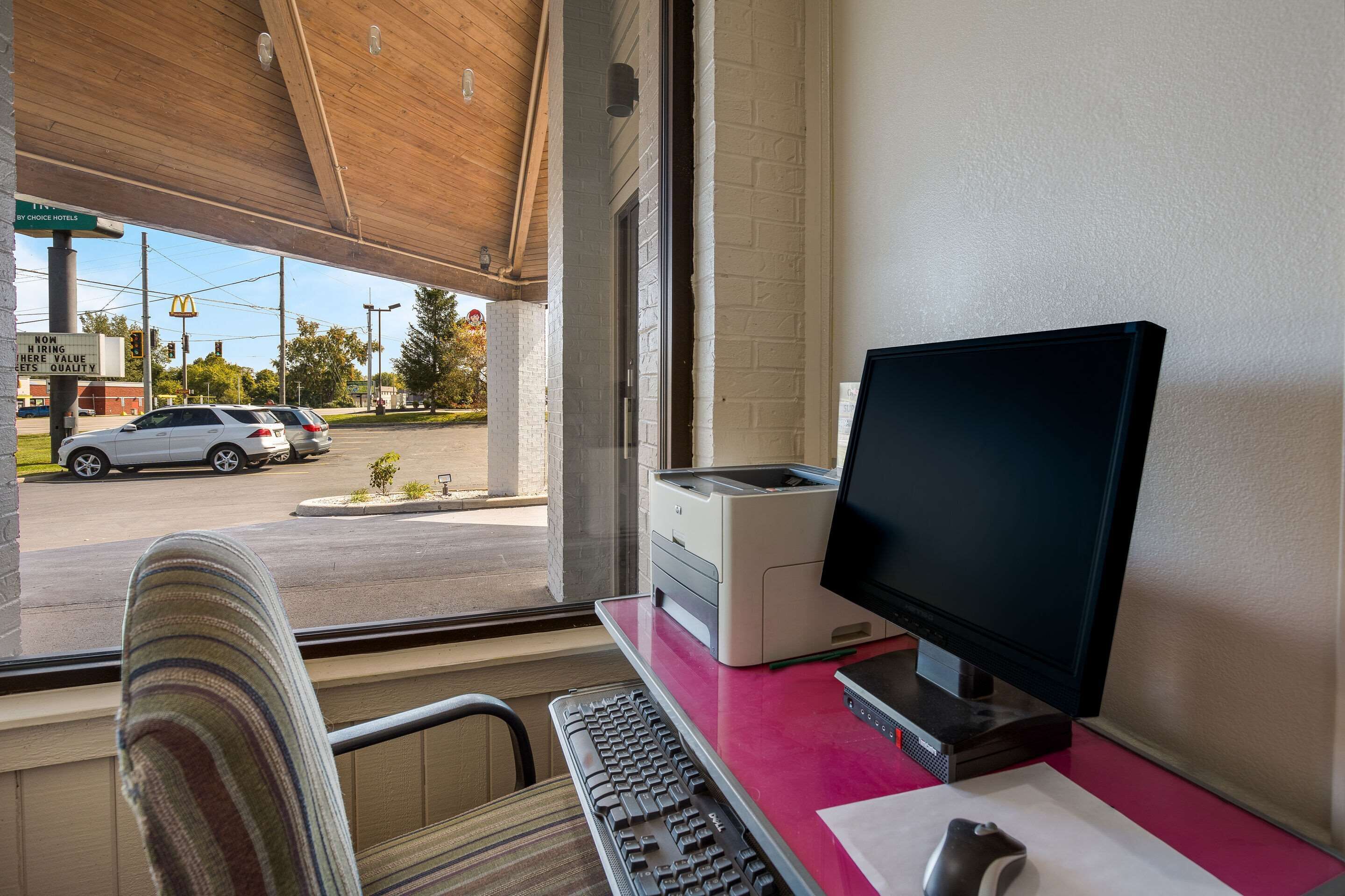A hotel room with a desk, a computer, and a window overlooking a street with cars and a McDonald's sign.