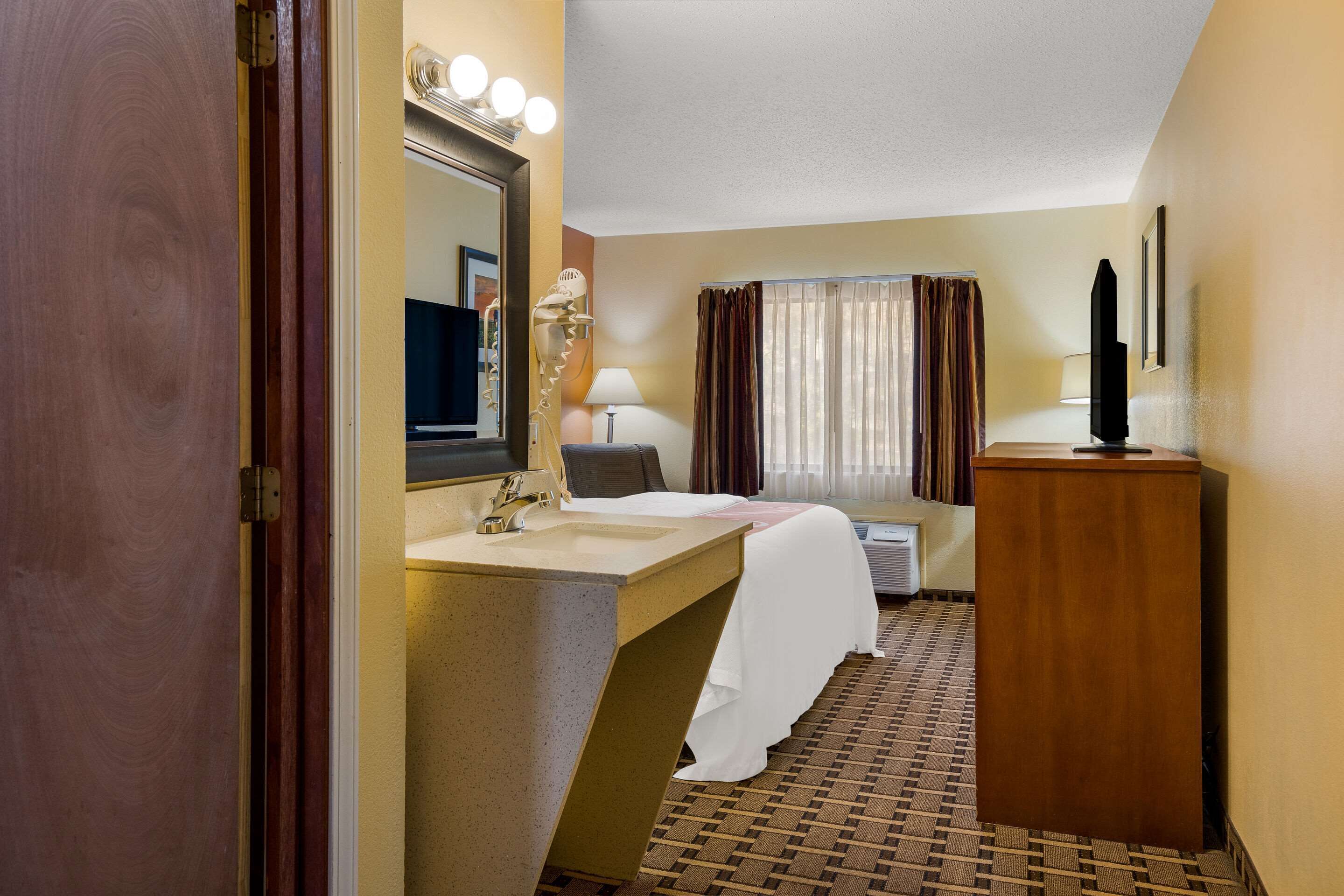 A hotel bathroom with a sink, mirror, vanity, and a shower area.