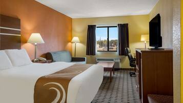 Une chambre d’hôtel avec un grand lit, deux tables de chevet avec des lampes, un bureau avec une chaise, une télévision et une fenêtre avec des rideaux.