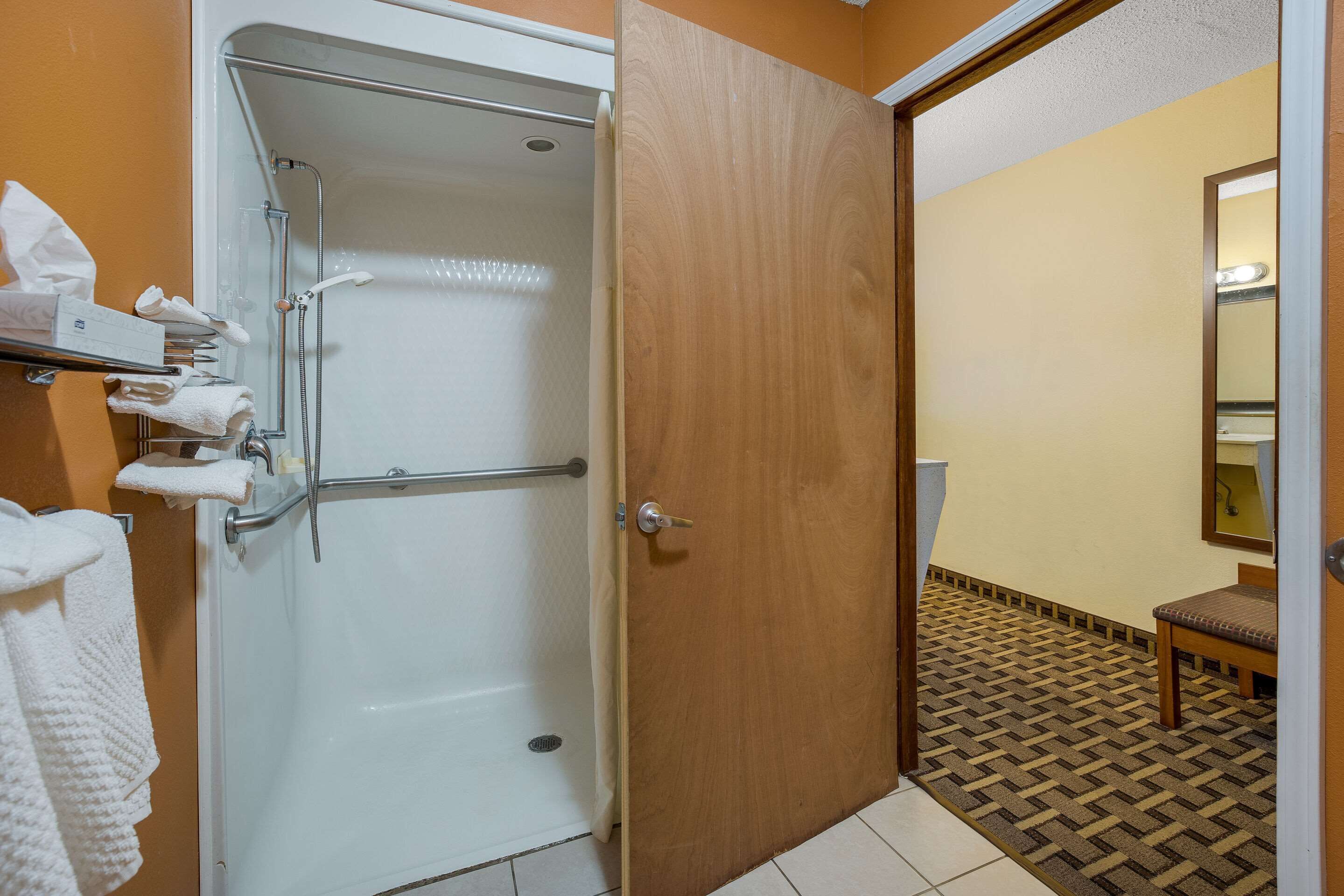 A bathroom with a shower, a wooden door, a bench, and a mirror.