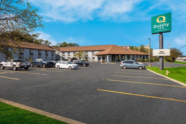 A Quality Inn by Choice Hotels with a parking lot, several cars, and a clear blue sky.