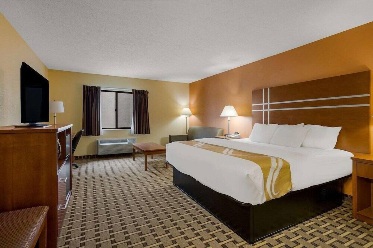A hotel room with a bed, desk, chair, TV, lamps, and a window with curtains.