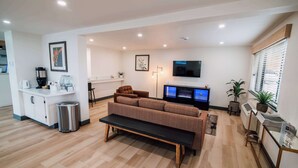A modern living room with a sofa, a coffee table, a TV, and a kitchen area with a sink and countertop.