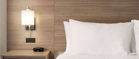 A neatly made hotel room with a wooden headboard, a bedside table with a lamp, and a bed with white bedding.