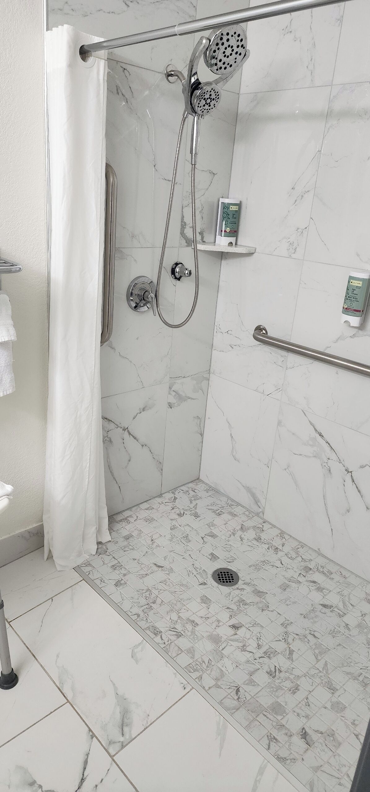 A shower area with a handheld showerhead, a handheld shower attachment, and a handheld shower head with a rain shower attachment.