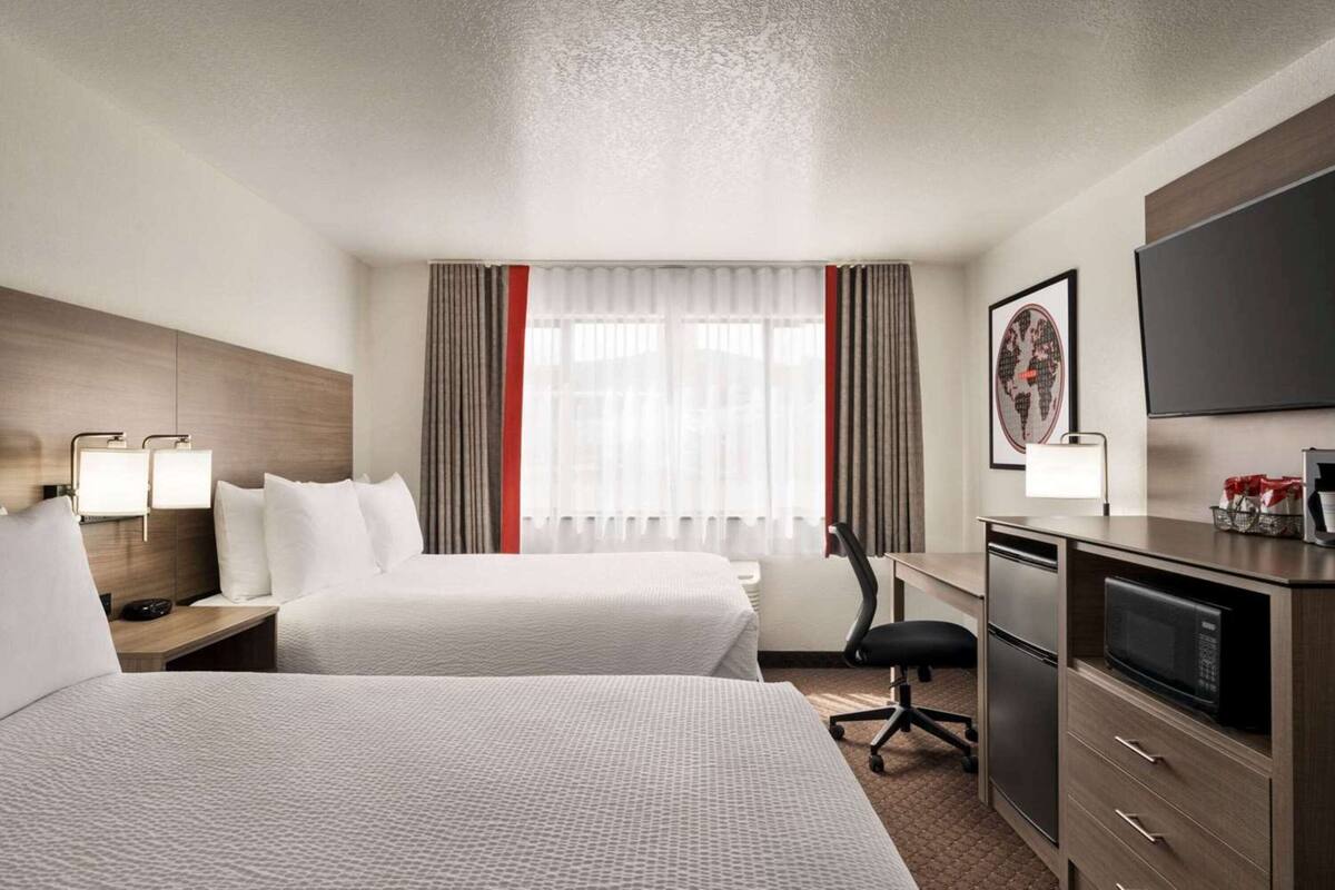 A hotel room with two beds, a desk with a microwave, a chair, and a TV on the wall.