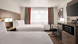 A hotel room with two beds, a desk with a microwave, a chair, and a TV on the wall.