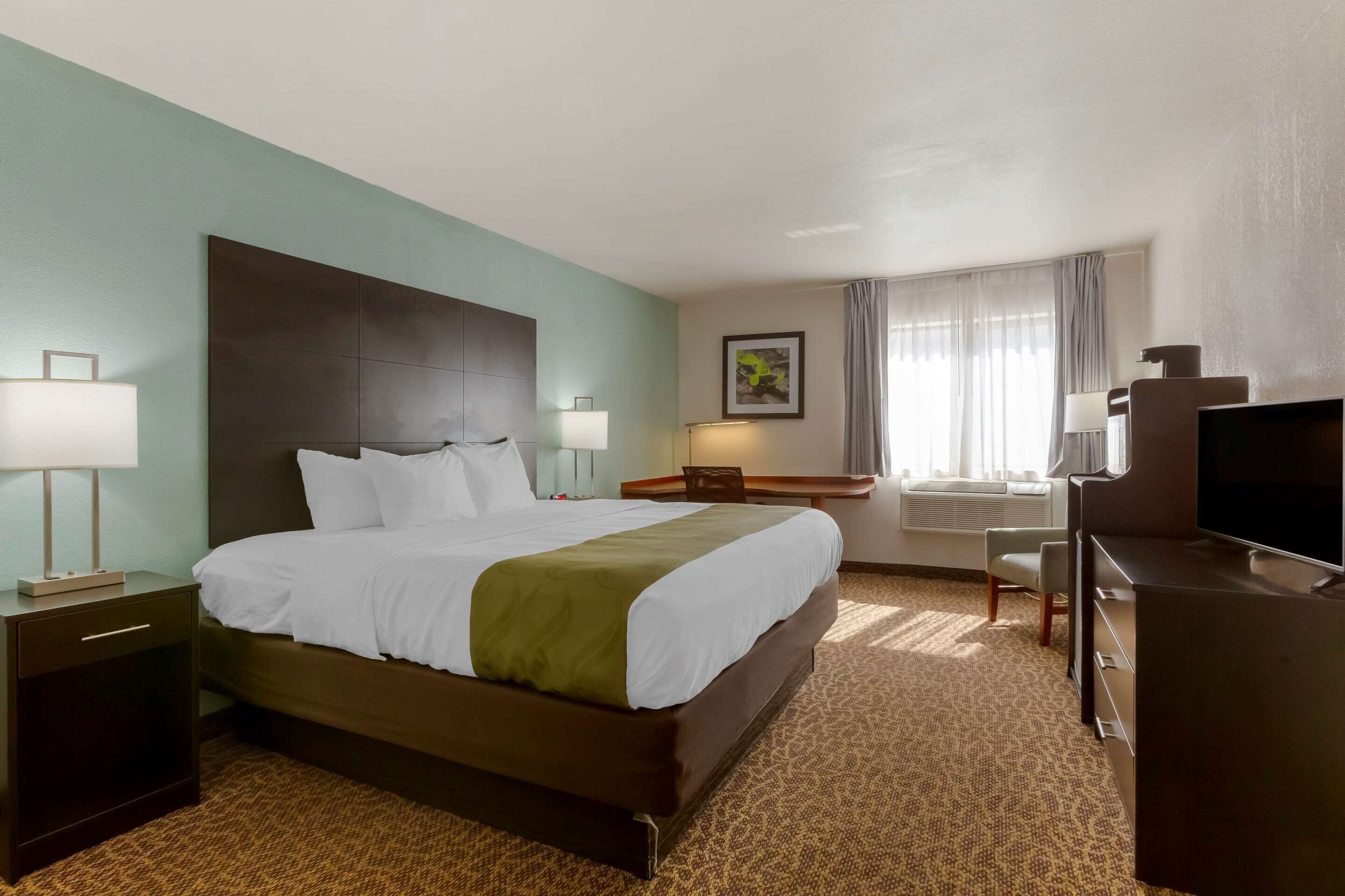 A hotel room with a large bed, a desk with a chair, a television, and a window with curtains.
