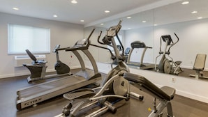 A modern gym with multiple exercise machines, a large mirror, and a window with blinds.