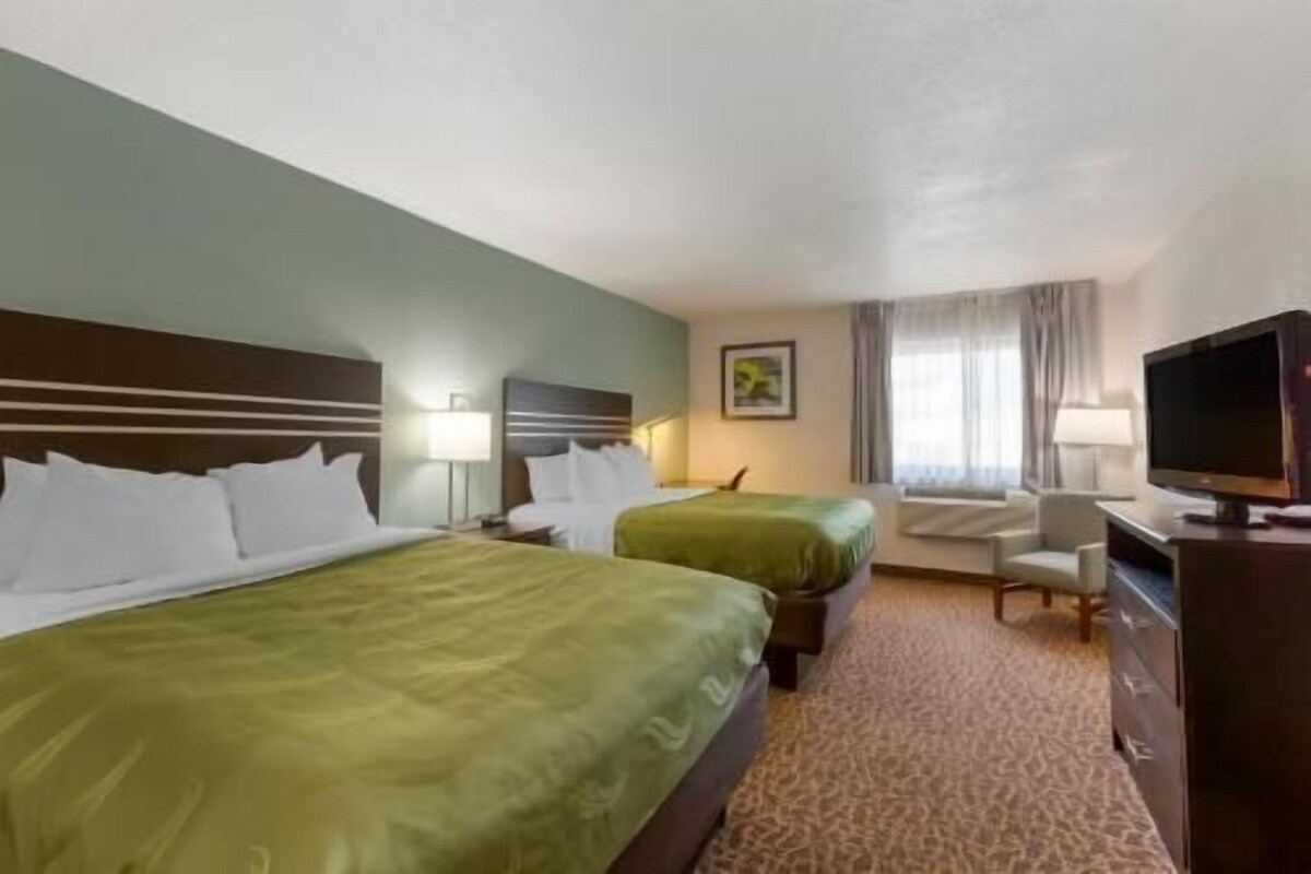 Quarto de hotel com duas camas, televisão, escrivaninha e uma cadeira.