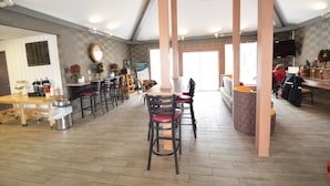 A spacious cafe with wooden tables and chairs, a large window, and a television mounted on the wall.