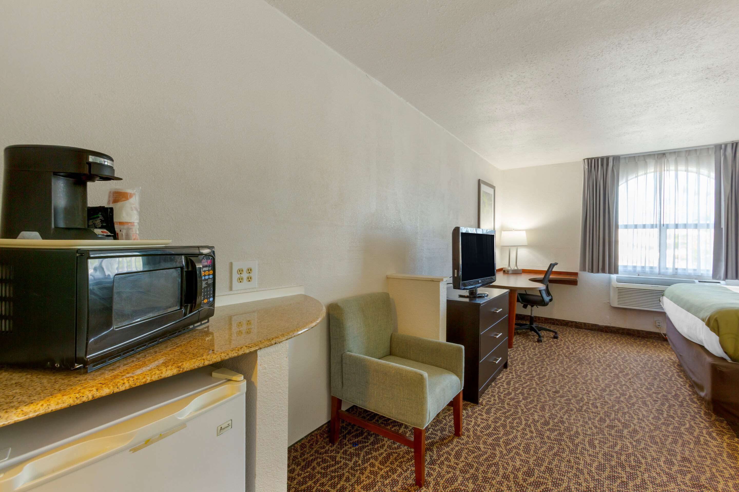 Una habitación de hotel con kitchenette, una cama, un escritorio con computadora y una silla.
