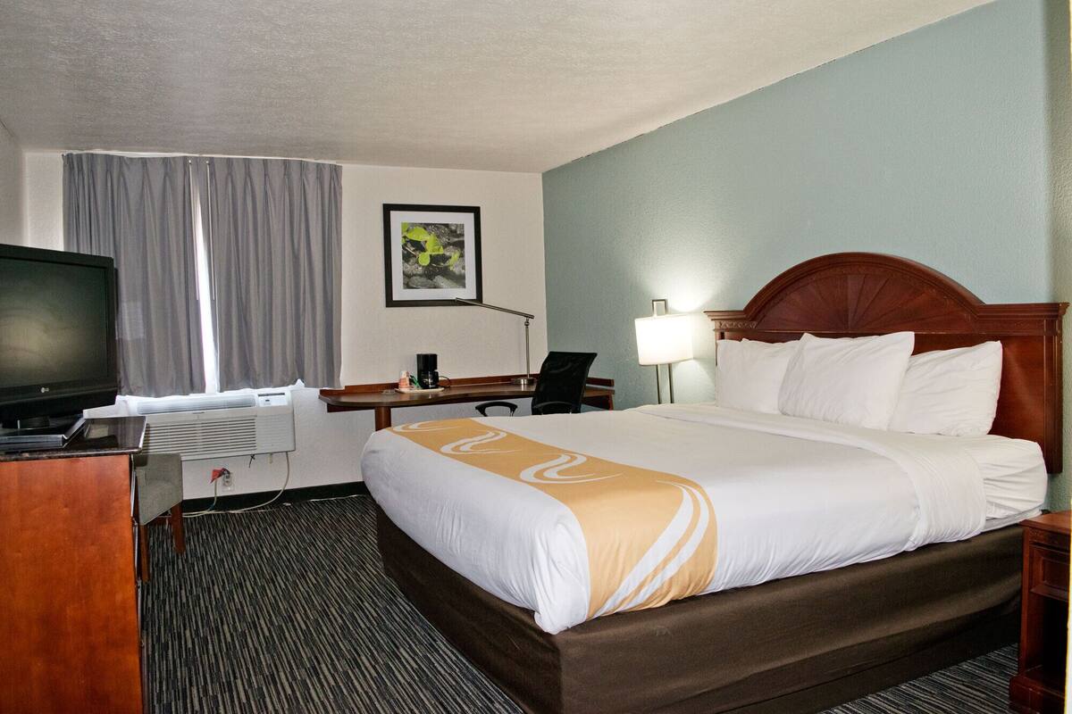 A hotel room with a bed, a desk with a computer, a TV, and a lamp.
