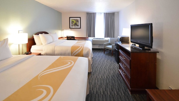 A hotel room with two beds, a TV, a desk, and a chair.